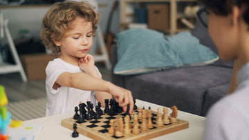 Small child playing chess on a coffee table with woman