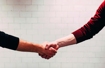 Image of two hands locked in a firm handshake against a white brick background.