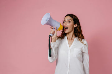 Woman in white t-shirt holding a megaphone against a light pink background.
