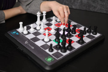 A picture of an electronic chess board with pieces, and a hand holding one figure.